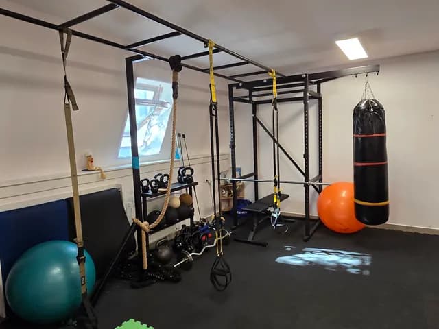 A stúdió eszközparkja: fém rack TRX szalagokkal, boxzsák, kettlebellek, pad és gimnasztikai labdák