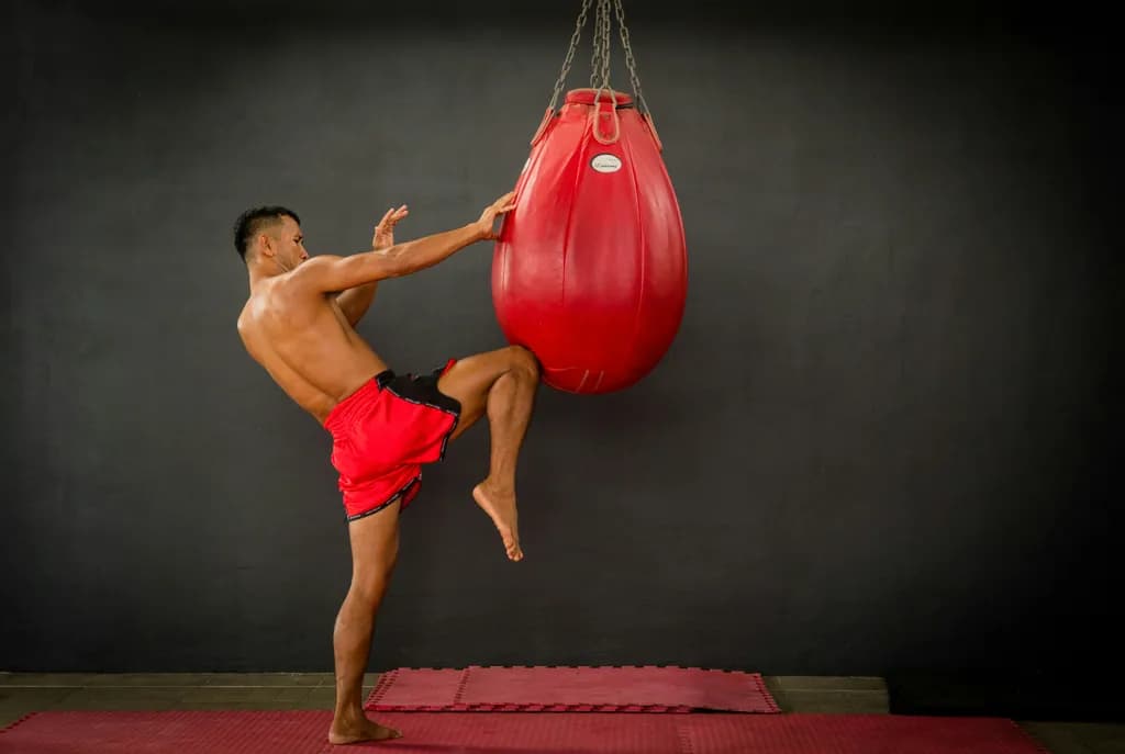 Thai bokszoló magas rúgással találja el a piros boxzsákot az edzőszőnyegen